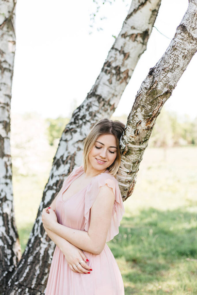 Portrait of attractive woman wearing pink dress near birch tree at summer green park. - Photo, image