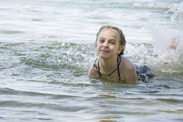 No verão, em um dia ensolarado brilhante, uma menina em um maiô banha no lago
. - Foto, Imagem