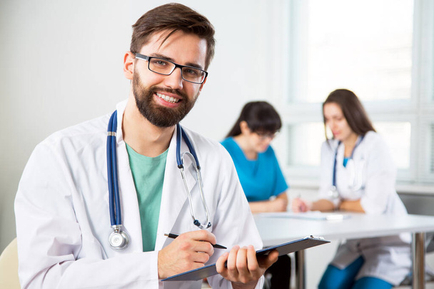 Portrait of a young doctor in a clinic with colleagues on the background - Foto, afbeelding
