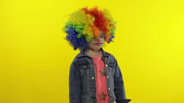 Kleines Kindermädchen Clown in Regenbogenperücke wütend stehend und wartet auf etwas. Halloween - Filmmaterial, Video
