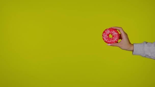 Vrouwelijke hand houdt een rode smakelijke en verse donut, gele achtergrond - Video