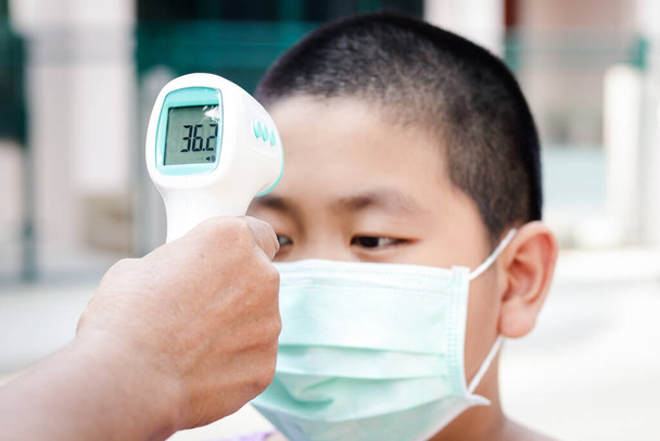 Азиатский мальчик был обследован с помощью цифрового термометра. Чтобы предотвратить коронавирусную инфекцию
 - Фото, изображение