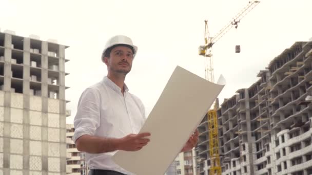 Architect or engineer working in hard hat browsing building project of construction site with blueprint plan - Video, Çekim