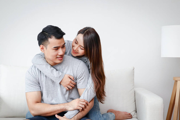 Νεαρά Ασιατικά ζευγάρια αγκαλιάζονται χαρούμενα στον καναπέ του σαλονιού στο σπίτι. Η ιδέα της δημιουργίας μιας οικογένειας παντρεμένων ζευγαριών. Κοινωνική απόσταση - Φωτογραφία, εικόνα