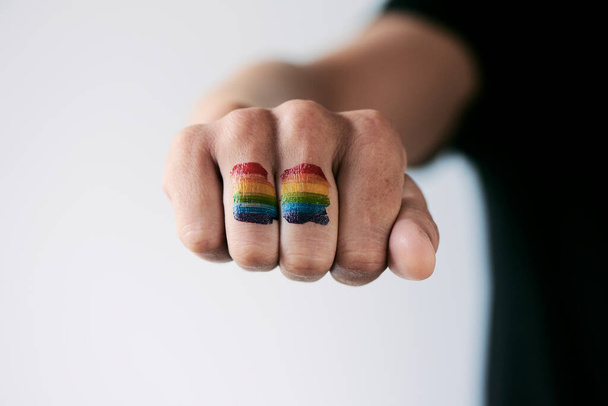close-up de uma bandeira do arco-íris no punho de uma jovem pessoa caucasiana, contra um fundo esbranquiçado
 - Foto, Imagem