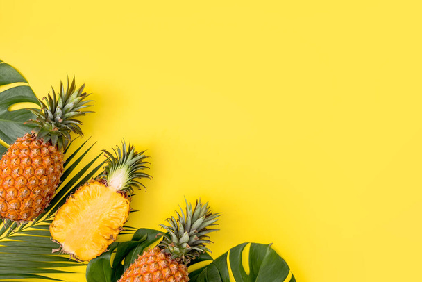 Beautiful pineapple on tropical palm monstera leaves isolated on bright pastel yellow background, top view, flat lay, overhead above summer fruit. - Foto, Imagem