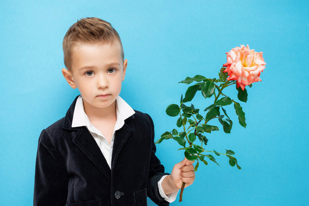 Задумчивый задумчивый четырехлетний мальчик в черной куртке и белой рубашке держит розу
 - Фото, изображение