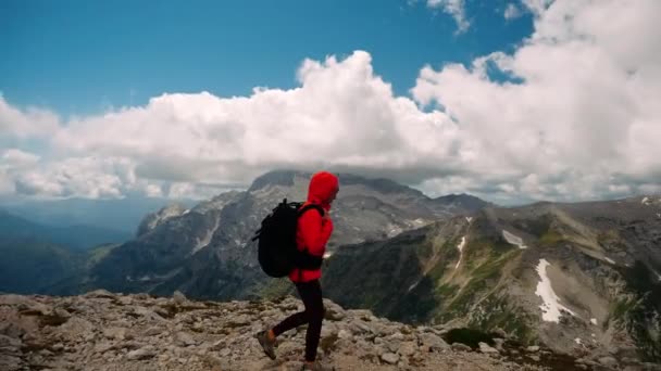 Zijaanzicht van wandelende toerist veroverd en beklommen piek in oranje jas en rugzak, stoppen en kijken met plezier op prachtige berglandschap van de Kaukasus bergen onder wolken. - Video