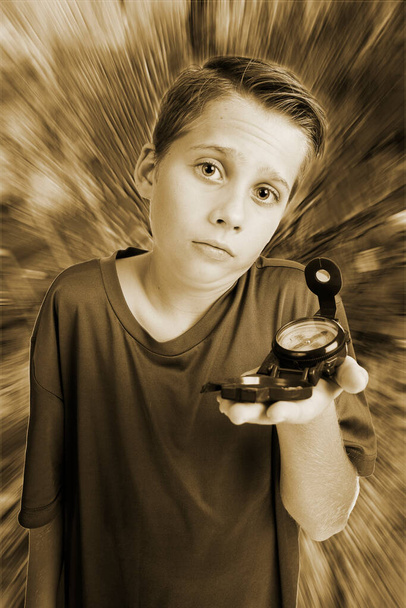 Monochrome image of a 12-year-old Caucasian boy in an elevated, wide-angle three-quarter view with a compass on his left hand, looking at the camera helplessly against a radially distorted background. - Photo, Image