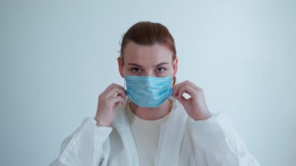 doctor at work, female medical staff member in gloves puts on protective suit, mask and goggles during pandemic due to coronavirus to examine patients with ill health and symptoms of illness - Felvétel, videó
