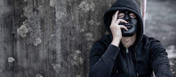 Mystery man met zwart masker met hoodie jas zittend op verlaten gebouw zich moe en gestrest voelen. Depressie (depressieve stoornis) of concepten voor geestelijke gezondheidsproblemen. - Foto, afbeelding