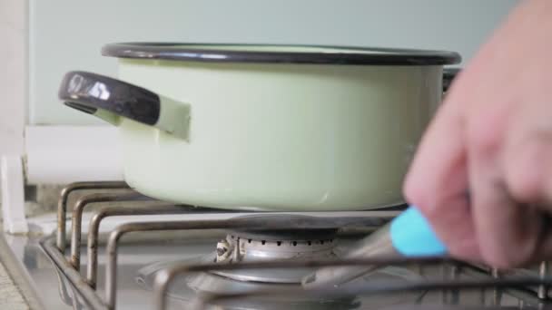 Green pot is on the gas cooker. The hand of a man holding a blue stove lighter approaches by lighting the fire under the pot with a spark. Man's preparing meal - Footage, Video