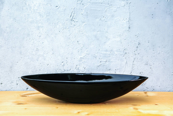black oval bowl on wooden table with grey background - Zdjęcie, obraz