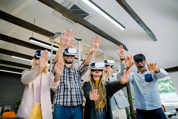 Happy multiethnic team of young people in casual colorful clothes trying virtual reality glasses for work in creative office. Young people using new technology for startup, 3d visualisation - Foto, Imagen