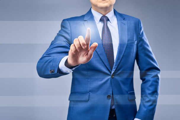 A businessman in a blue suit on a gray-blue background presses a finger in front of him on the running lane. The concept of choice in business, making the right decision. - Фото, зображення