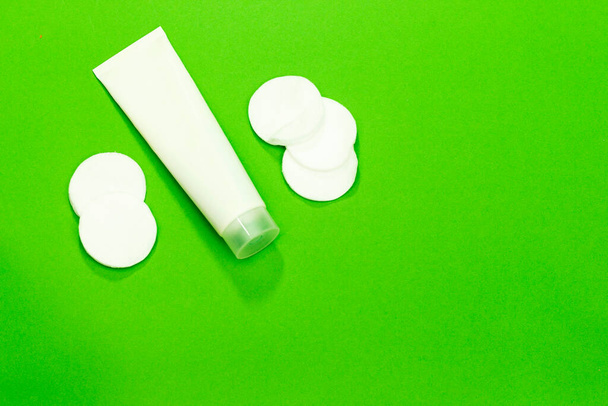 Tube crème et tampon de maquillage en coton sur fond vert - Photo, image