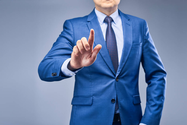 A businessman in a blue suit on a gray-blue background holds his index finger in front of him simulating a tap. Layout for subsequent design. The concept of choice in business. - Foto, Bild