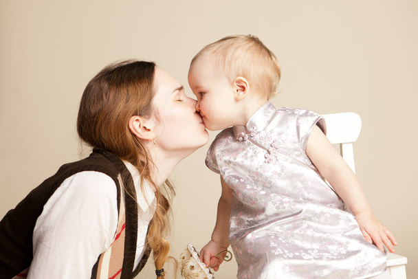 mom kisses little kid girl with short hair in dress with small toy umbrella - Foto, imagen