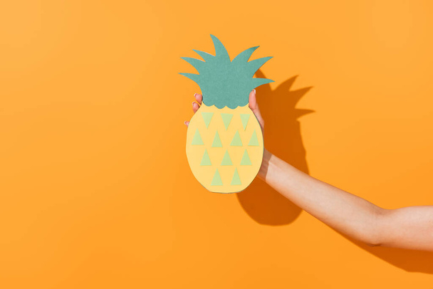 cropped view of young woman holding paper craft pineapple on orange  - Фото, зображення