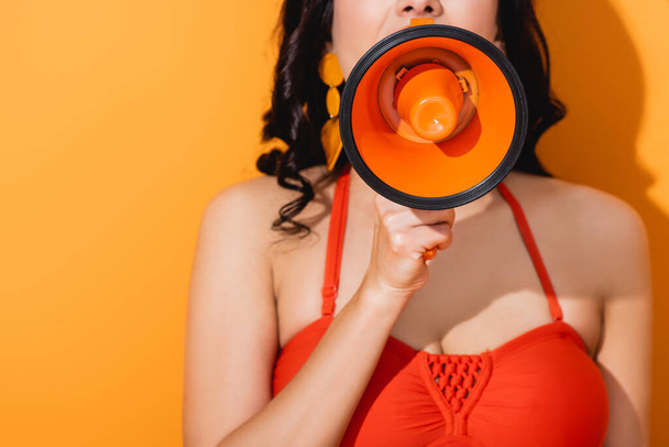cropped view of young woman screaming in megaphone on orange - Foto, immagini
