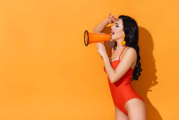 excited young woman in swimsuit holding megaphone on orange - Fotografie, Obrázek