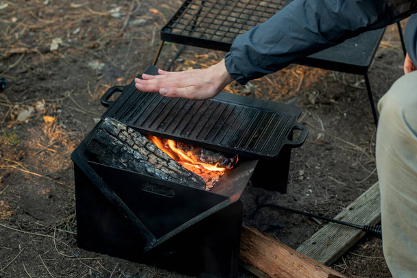 Βάζοντας τη φωτιά σε μια φορητή αναδιπλούμενη φωτιά για μια κατασκήνωση που μαγειρεύει σε πιάτο από χυτοσίδηρο - Φωτογραφία, εικόνα