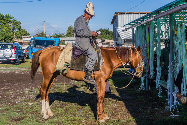 KARAKOL, KYRGYZSTAN - JULY 15, 2018: Local man riding a horse at the Sunday animal market in Karakol. - Zdjęcie, obraz