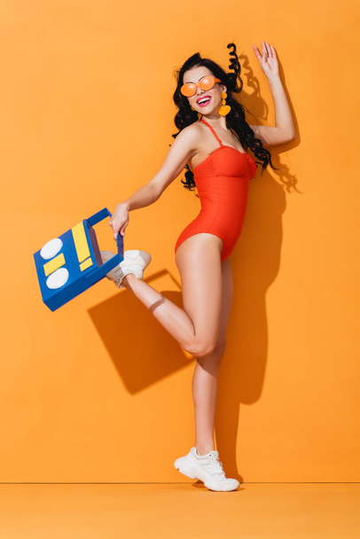 Spor ayakkabılı, güneş gözlüklü, mayolu, elinde kağıt kesikli müzik kutusu olan şık bir kadın. - Fotoğraf, Görsel