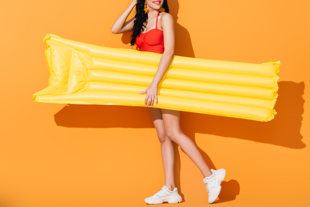 vista cortada da menina feliz no maiô e nos tênis que prendem o colchão inflável na laranja
  - Foto, Imagem