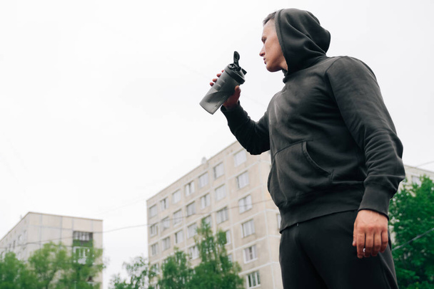 The athlete drinks a drink from a shaker during a workout. Fitness trainer man drinks sports supplements before exercise - Фото, зображення