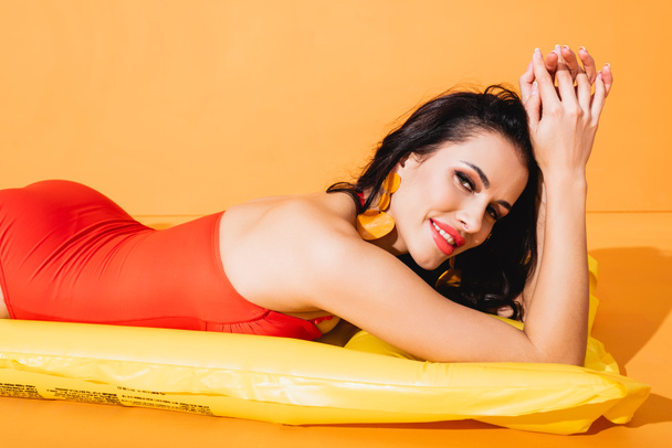 happy girl in swimsuit lying on inflatable mattress on orange  - Foto, immagini