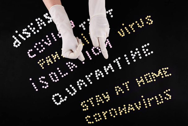 Two hands in medical gloves with fuck and fig gesture. Pandemic headline clipping words made of multicolored pills on black background.  - Foto, immagini