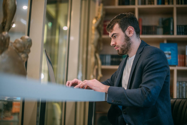 Een man werkt op een laptop in een kantoor of coworking. Jonge zakenman in stijlvolle kleding met een computer op een moderne werkplek. - Foto, afbeelding