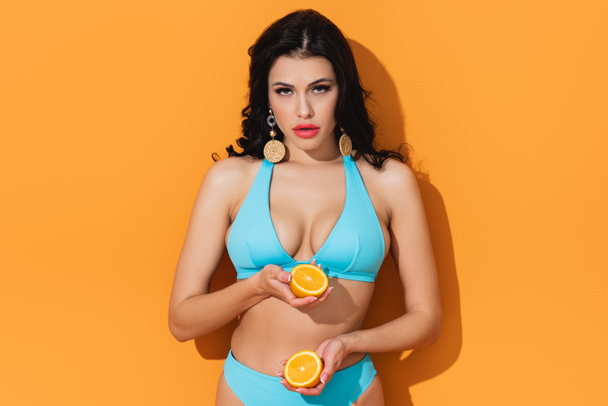 beautiful woman in bathing suit holding fruit halves on orange  - Фото, зображення