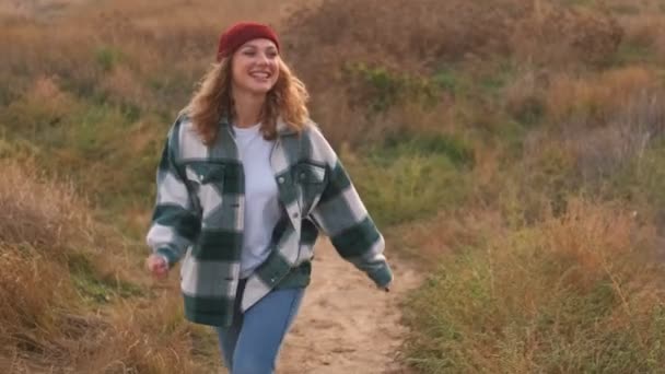 Joyful blonde woman wearing hat and plaid shirt having fun and looking around while walking outdoors - Filmagem, Vídeo