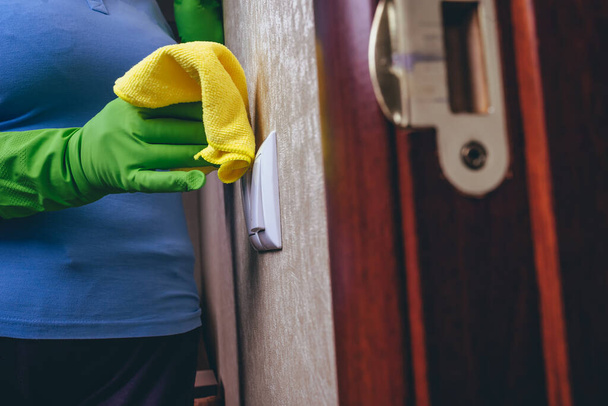 Cleaning in the house. A girl in green gloves wipes the electricity switch with a yellow cloth. cleaning from dust. Cleaning of surface. Blue T-shirt and experienced worker. close up. - Photo, Image