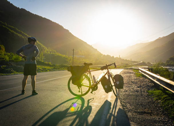Erkek bisikletçi yolda dikilir ve bisikletine bakar, turneye çıkar. Spor ve ekolojik seyahatin keyfi. Değişken ulaşım yolları. Salgın hastalık sonrası seyahat. 2020 - Fotoğraf, Görsel