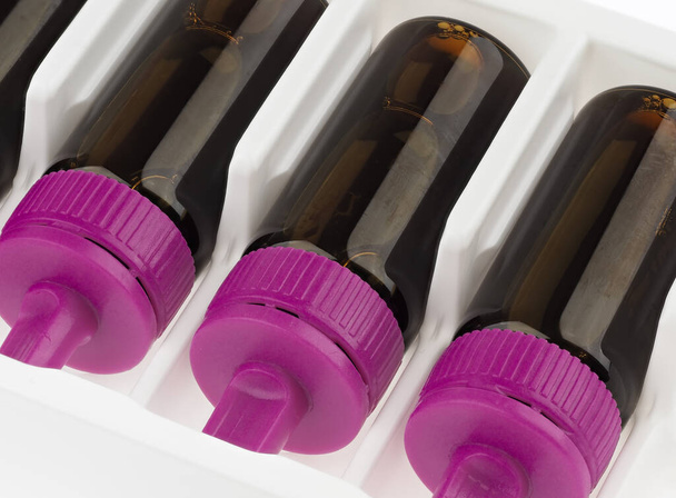 Коричневые флаконы с фиолетовой крышкой, наполненной коричневой жидкостью. Пищевая добавка
.    - Фото, изображение