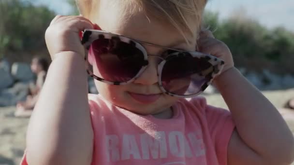 Młoda dziewczyna nosi duże okulary słoneczne na plaży - Materiał filmowy, wideo