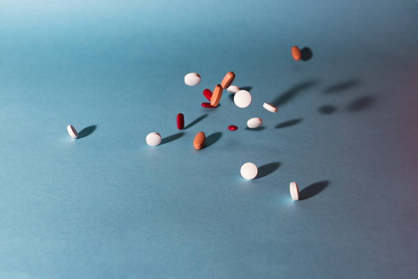 Archivbild eines Bündels verschiedener Pillen, das auf blauem Hintergrund herunterfällt. Es ist niemand auf dem Bild. - Foto, Bild