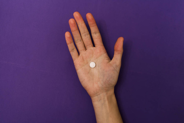 Stock photo of someones hand pinching a single tablet on a purple background. The person is unrecognizable. - Фото, изображение