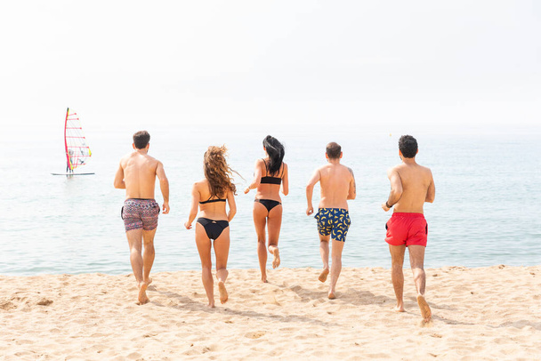 Friends having fun on the beach in Barcelona - Multiracial group of best friends enjoying summer time together running to take a swim - Happiness and friendship during a travel in Spain - Photo, Image
