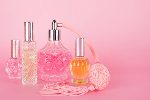 Különböző átlátszó parfümös üvegek rózsaszín háttérrel. Aromás esszenciás üvegek. Parfümök, kozmetikumok, illatszerek gyűjteménye. Szabad hely a szövegnek - Fotó, kép