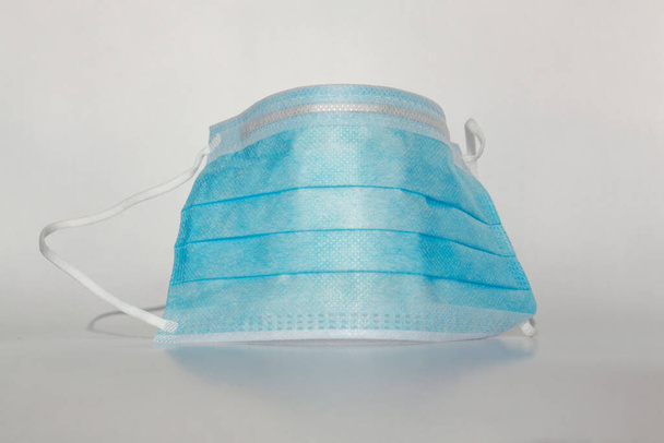 Egyetlen izolált kék orvosi maszk a vírus védelmére fehér alapon. A sebészeti maszk a 2020-as Coronavirus (covid-19) betegség elleni védelem szimbóluma. - Fotó, kép