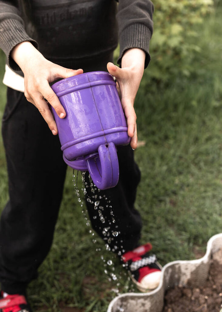 A child watering a flower bed with a baby watering can - Фото, изображение