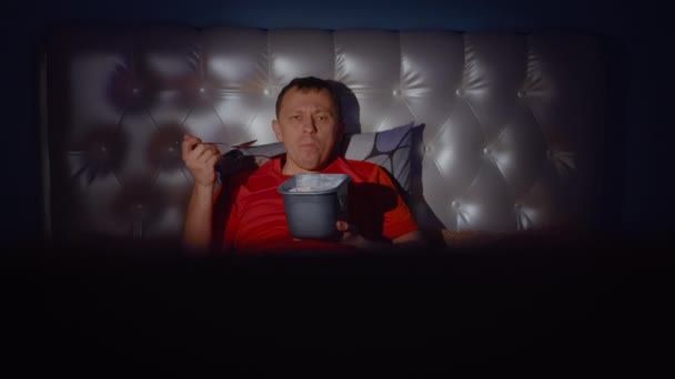 Der Kerl genießt den Abend vor dem Fernseher mit einem Verd leckerem Eis - Filmmaterial, Video