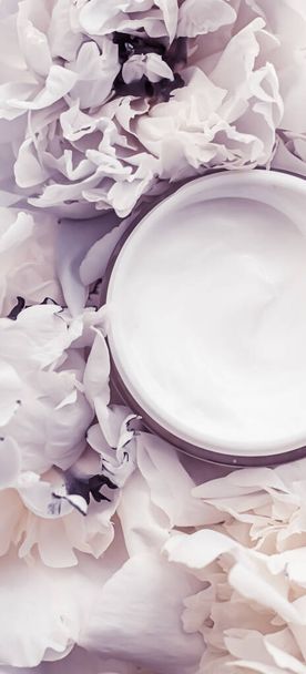 Pot de crème cosmétique de luxe comme produit de routine anti-âge sur fond de fleurs de pivoine, hydratant pour le corps et marque de beauté
 - Photo, image