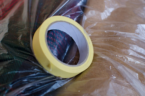 keltainen kreppa-teippi, maalauksessa käytetty maalarinteippi peittämään alueita, joille maalia ei haluta sängyssä läpinäkyvällä muovikalvolla päällystetyssä huoneessa, lähikuva - Valokuva, kuva