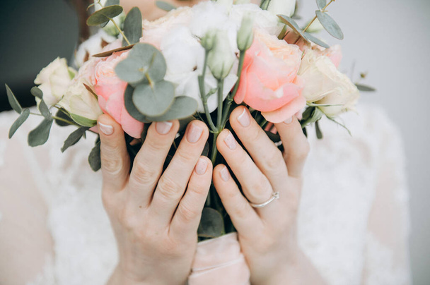 Die Hände der Bräute halten einen Blumenstrauß vor hellem Hintergrund. Strauß und Hände in Großaufnahme, das Gesicht der Bräute ist nicht zu sehen - Foto, Bild