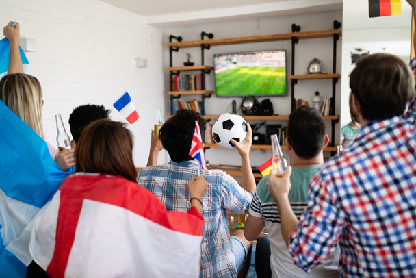 Fröhliche und fröhliche Gruppe von Freunden, die sich Olympische Spiele zu Hause im Fernsehen anschauen - Foto, Bild
